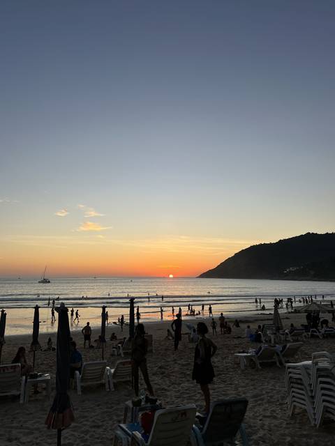 People on a beach at sunset with a hilly landscape in the background.