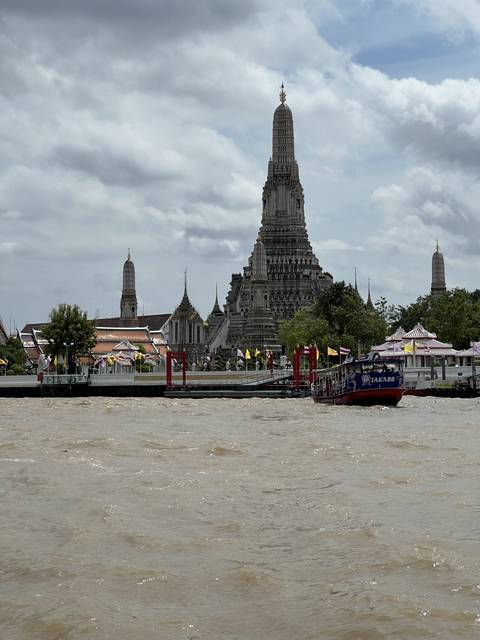 Temple structures along a riverbank with boats.