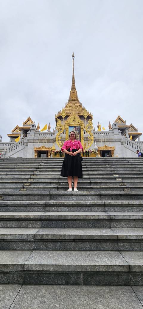 Woman in traditional dress on temple steps with golden architecture.