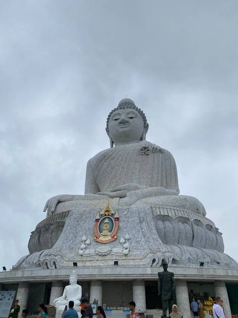       Large white Buddha statue with tourists around.
  