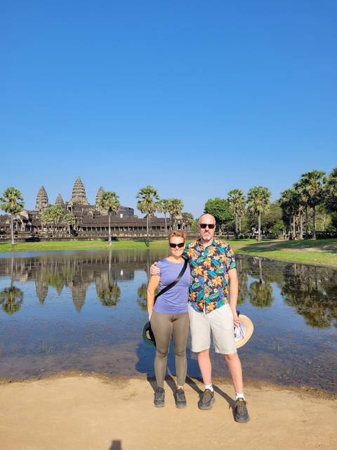Two people posing in front of a reflective pond with Angkor Wat in the background.