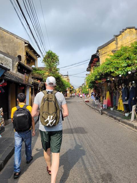 People walking down a bustling street lined with shops and greenery.