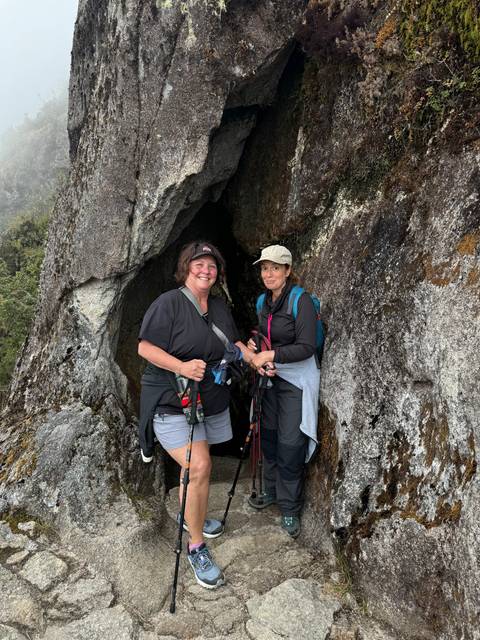 Two people standing in front of a rocky cave entrance.