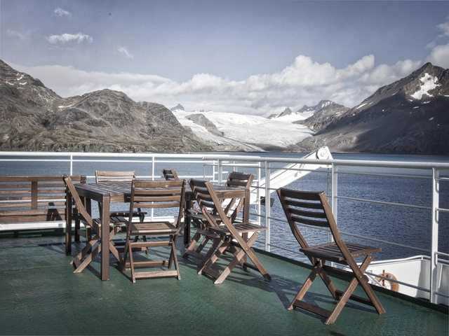       Deck of a ship with chairs offering a view of icy mountains and water.
  