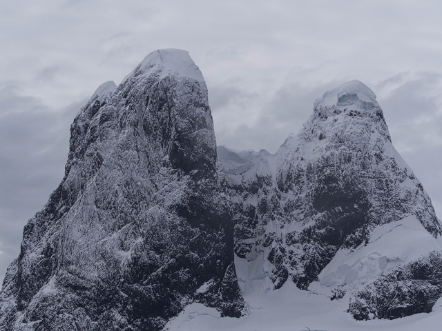       Majestic snow-covered mountain peaks under a cloudy sky.
  