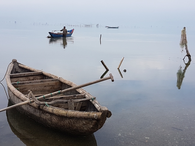 Wooden boats on a calm water body with people in the distance.