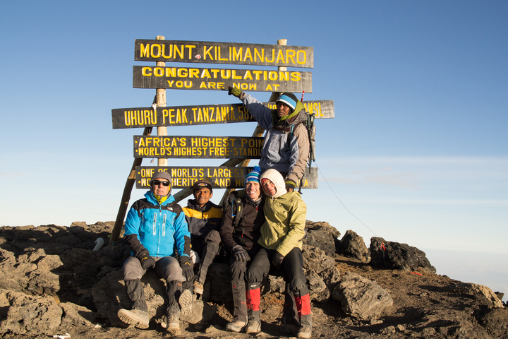       Group of hikers at the summit of Mount Kilimanjaro with signage.
  