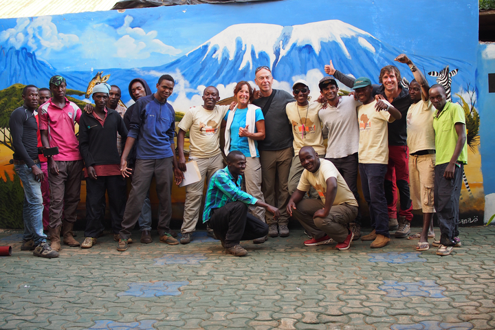       Group of people posing with a mural of Mount Kilimanjaro.
  