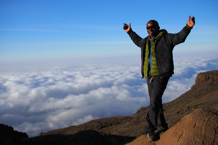       Hiker celebrating on a mountain with clouds in the background.
  