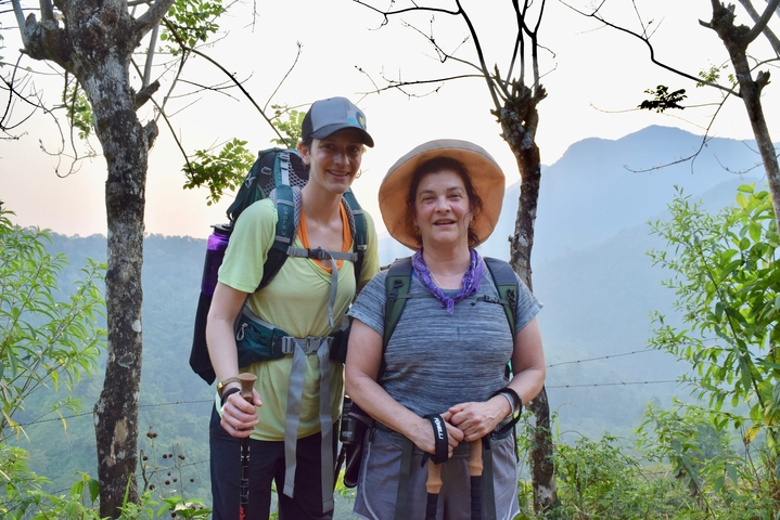       Two hikers posing on a forested trail with mountains in the background.
  