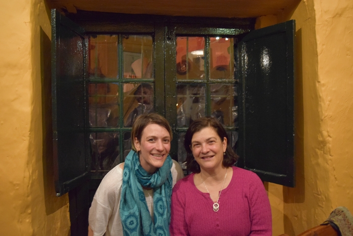 Two women indoors, one wearing a scarf and another in a pink sweater.