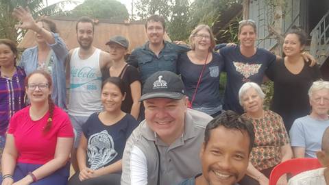       Group posing in front of colorful boats at a pier.
  