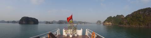       Deck of a boat with a Vietnamese flag, overlooking a bay with karst formations.
  