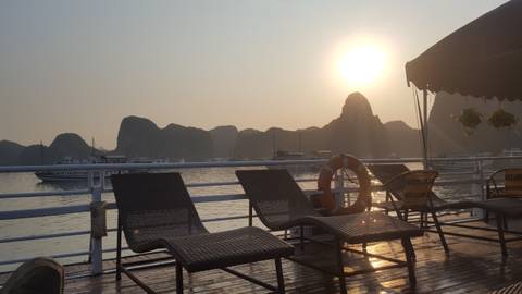       Sunset view from a cruise deck with lounge chairs and limestone formations.
  