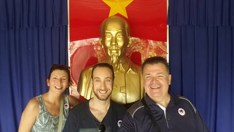       Group posing with a statue against a vibrant red backdrop.
  