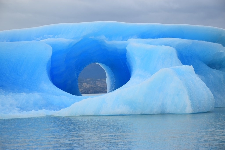 Arch of ice in a bright blue iceberg on water.