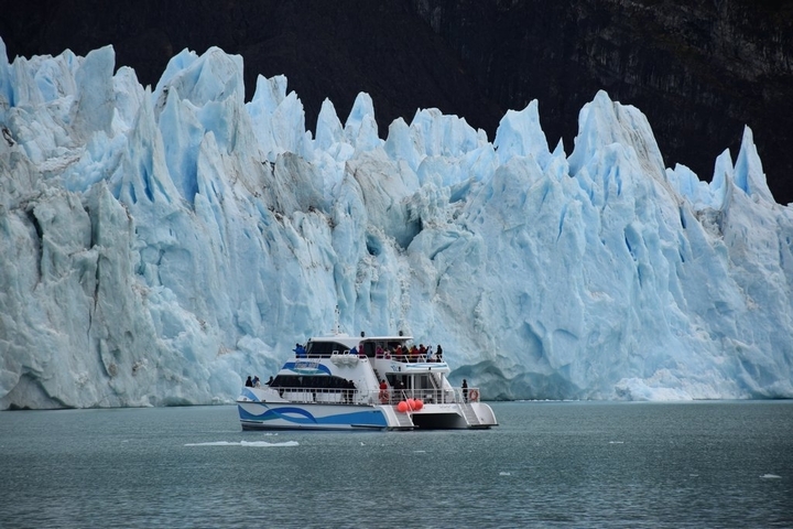 Boat cruising in front of an ice wall in a glacier.