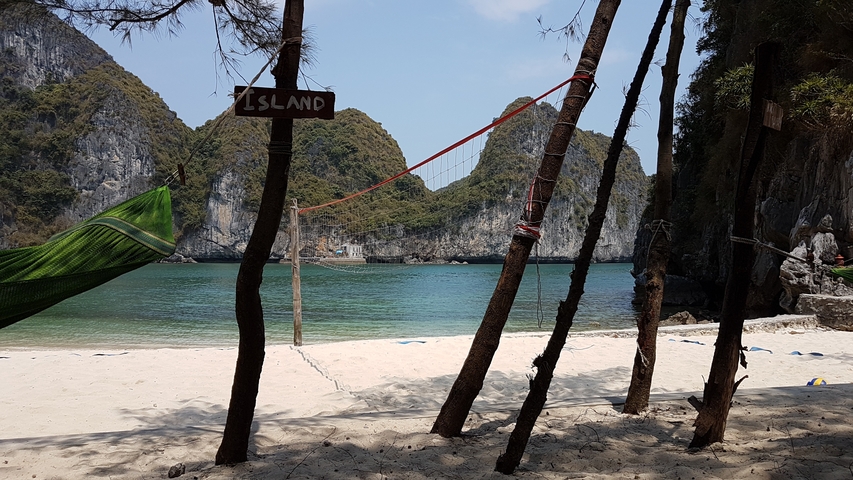 Beach with hammock and volleyball net, surrounded by cliffs.