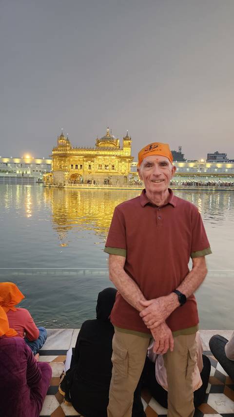 Man posing by water with a building in the background.