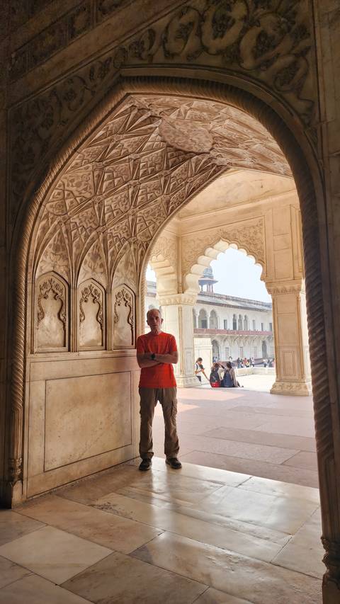       Man standing inside an ornately carved corridor.
  