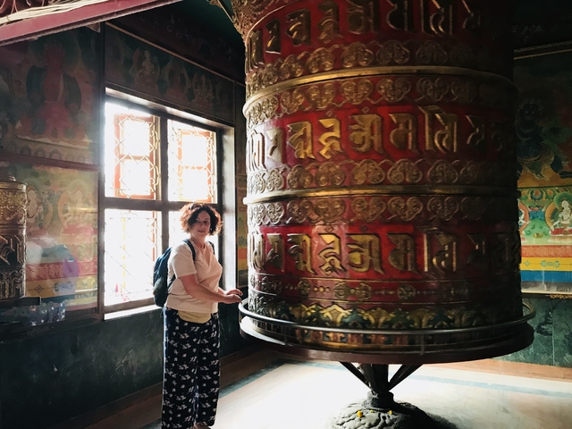A woman spinning a large prayer wheel indoors.