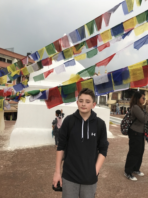A young boy standing in front of prayer flags and a stupa.