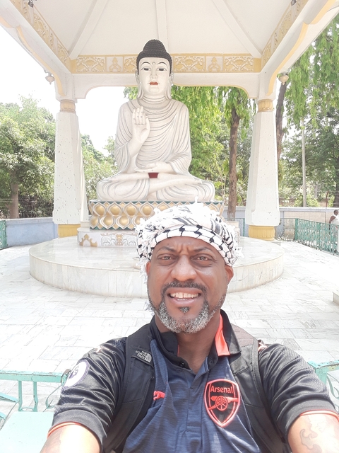       A smiling man in front of a white Buddha statue.
  