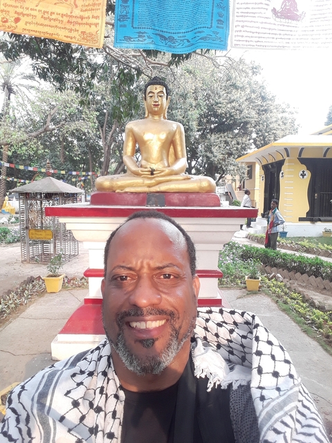       A man posing in front of a golden Buddha statue.
  