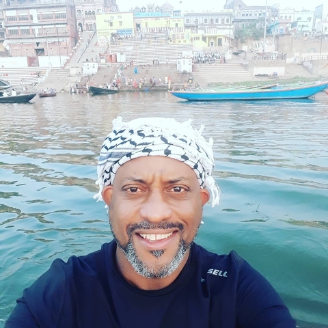      A man smiling in front of a river with boats.
  