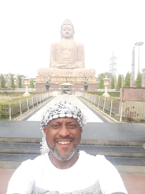       A man in front of a large seated Buddha statue.
  