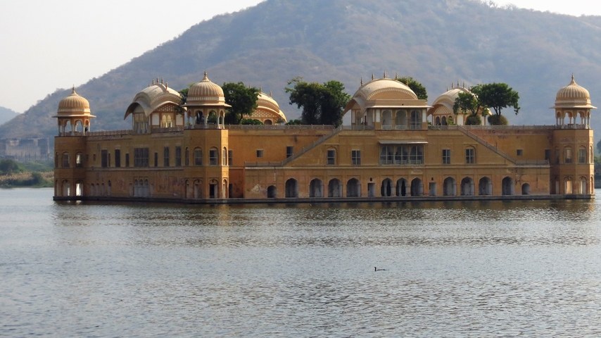       A grand palace surrounded by water with hills in the background.
  