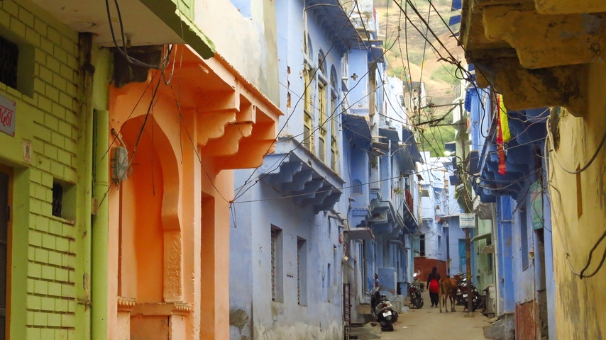       A narrow street in a vibrant neighborhood with colorful buildings and people walking.
  