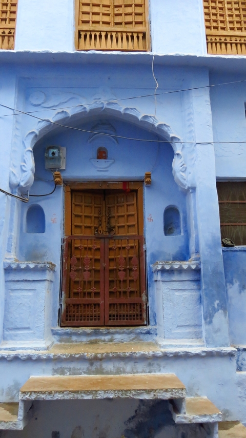       A blue painted building facade with a wooden door and ornamental details.
  