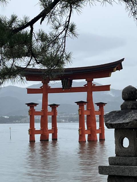       An iconic torii gate standing in water with mountainous background.
  