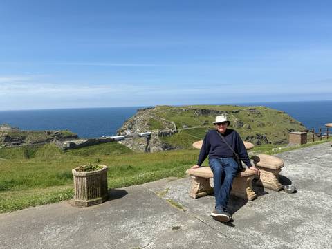 Person sitting on a bench overlooking the sea and green hills.
