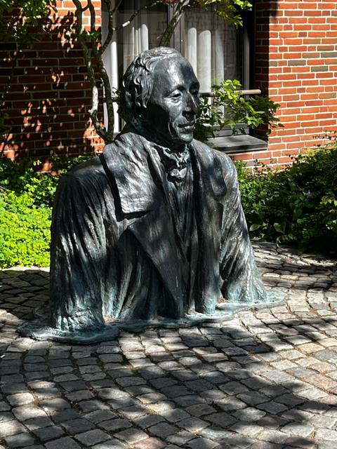       Bronze bust statue of a man in a park.
  