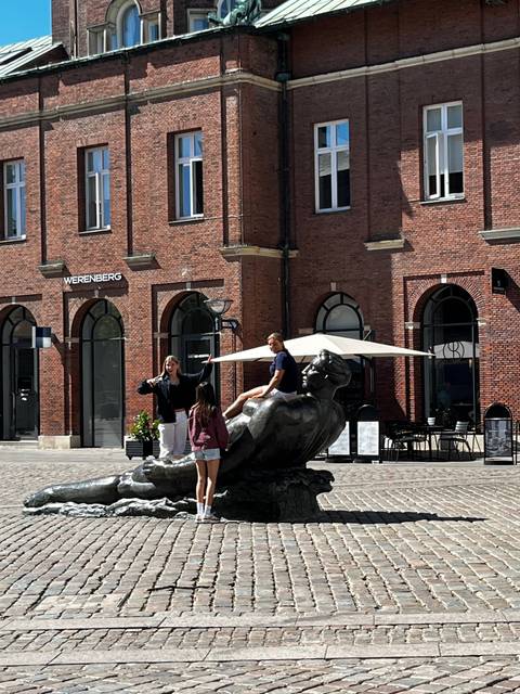       People at a fountain with a brick building background.
  