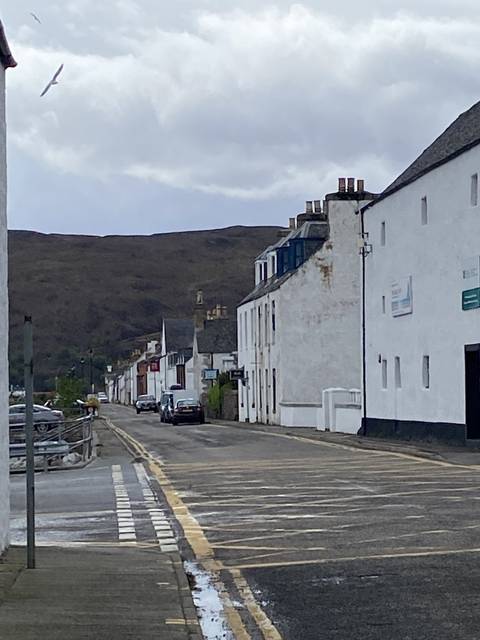       Row of buildings on a street with hills in the background.
  