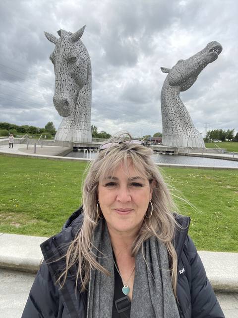       Person posing with a large sculpture of two horse heads.
  