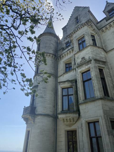       White stone building with turrets and trees in the foreground.
  