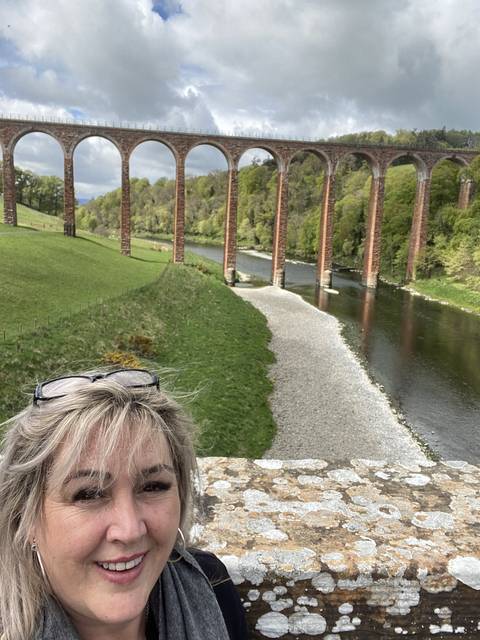       Person posing near a viaduct with multiple arches over a river.
  