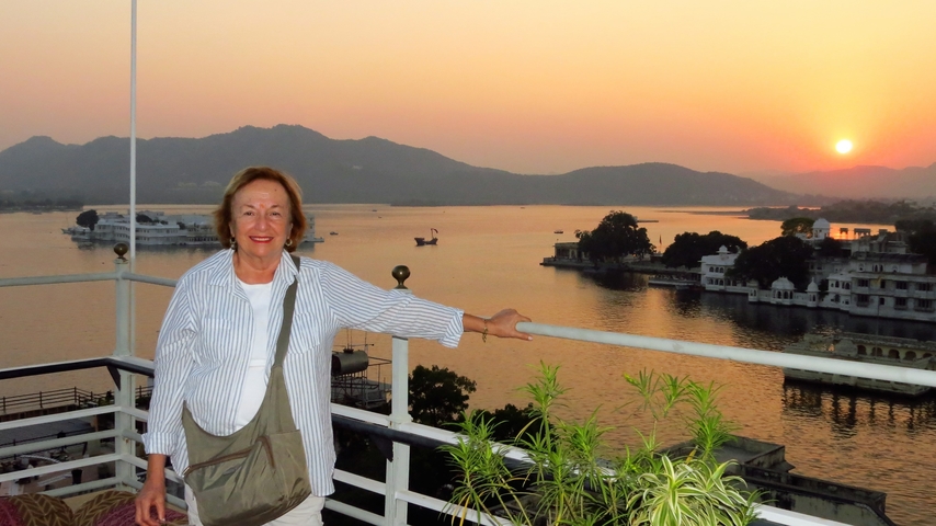 Woman on balcony overlooking a lake during sunset.