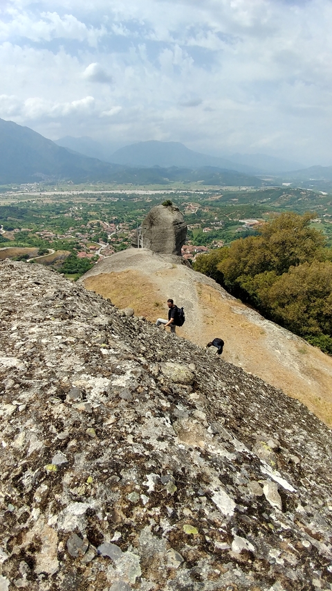       Hiker ascending a rocky cliff with a village in the background.
  