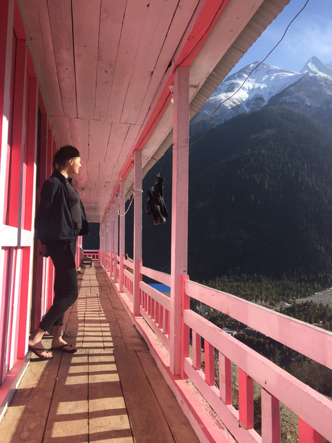       Person standing on a pink balcony with mountainous views.
  