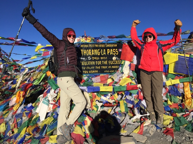       Two people celebrating at Thorong La Pass with prayer flags.
  