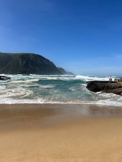       Sandy beach with waves crashing and mountains in the distance.
  