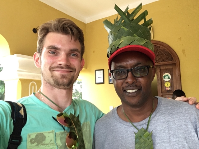 Two people smiling indoors, one wearing a traditional woven hat.