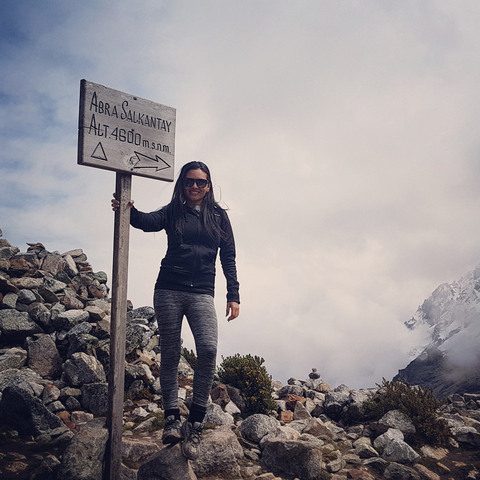 Smiling woman posing next to a sign at high altitude in the mountains.