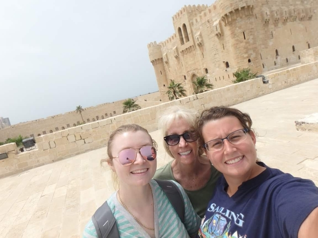 Three people posing with a castle-like structure.