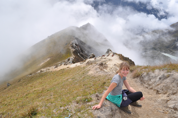 A person sitting on a grassy hilltop with clouds.